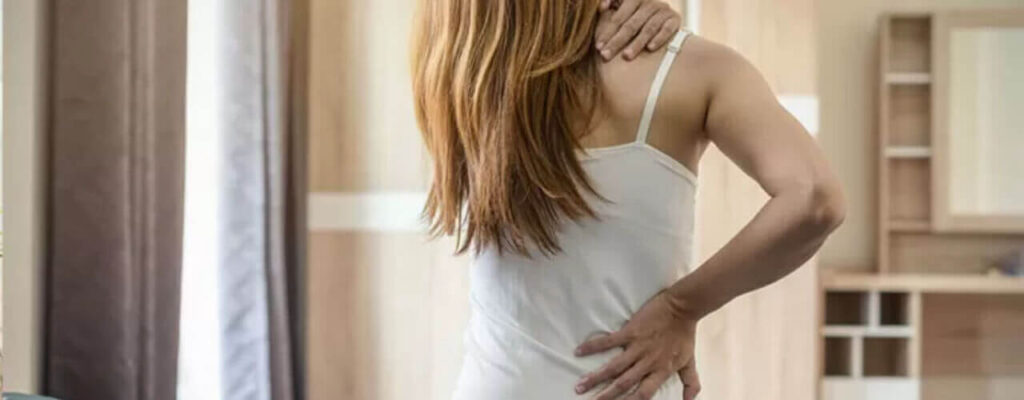 Female standing holding her neck and back indicating pain points.